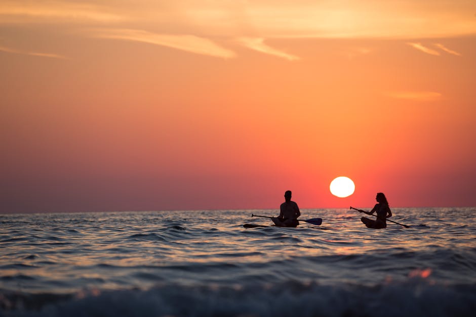 Silhouette of a couple paddleboarding on the ocean during a stunning sunset, capturing romance and adventure