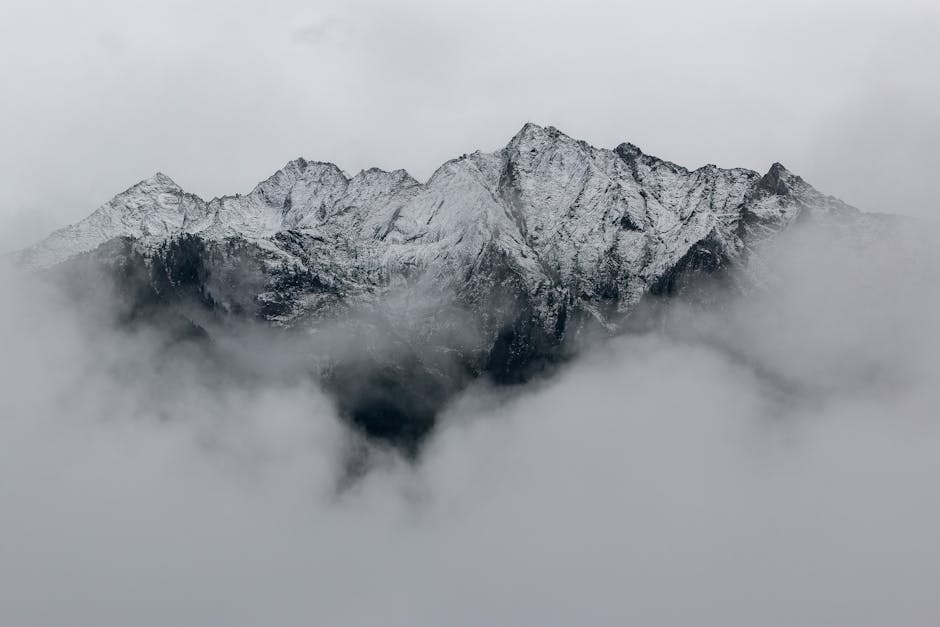 A breathtaking view of snow-covered mountain peaks surrounded by dense fog, creating a mystical landscape