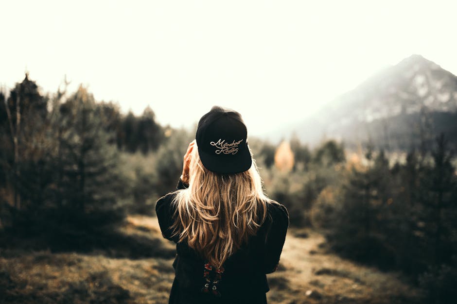 A woman in black cap and sweater enjoys a mountain view, embracing outdoor adventure.
